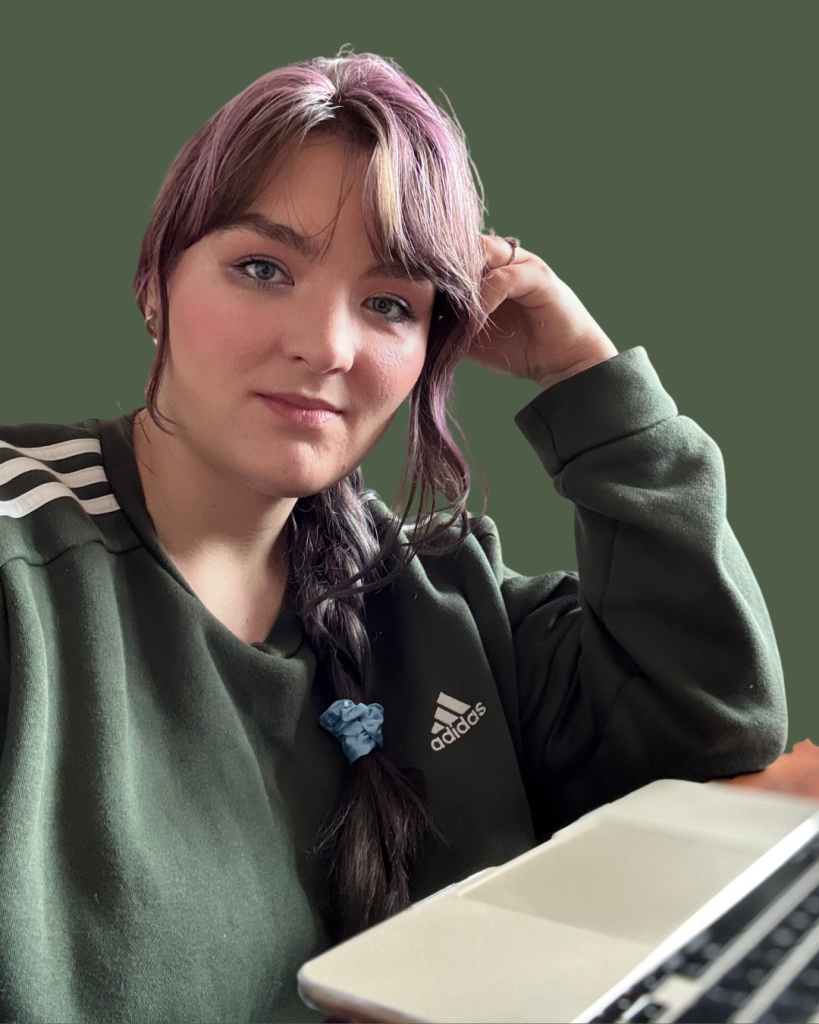 Kobieta z długimi włosami w zielonej bluzie z logo Adidas, siedząca przy laptopie.